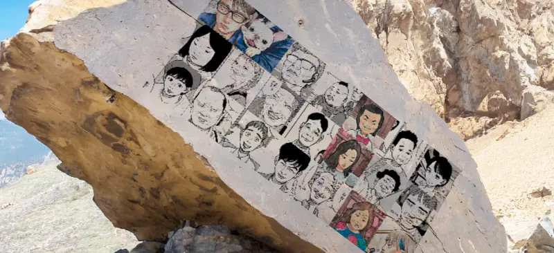 荒野にある岩に描かれた漫画「平和の国の島崎へ」の登場人物21名が一覧で並んだ画像